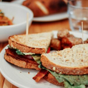 two sliced of sandwich on plate near bowl and drinking glass